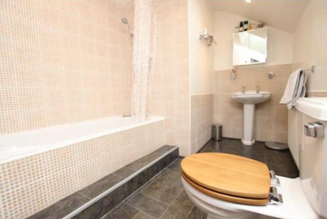 The bathroom before work — dated beige mosaic tiling, an old suite and a bath-shower combo under the sloped ceiling.