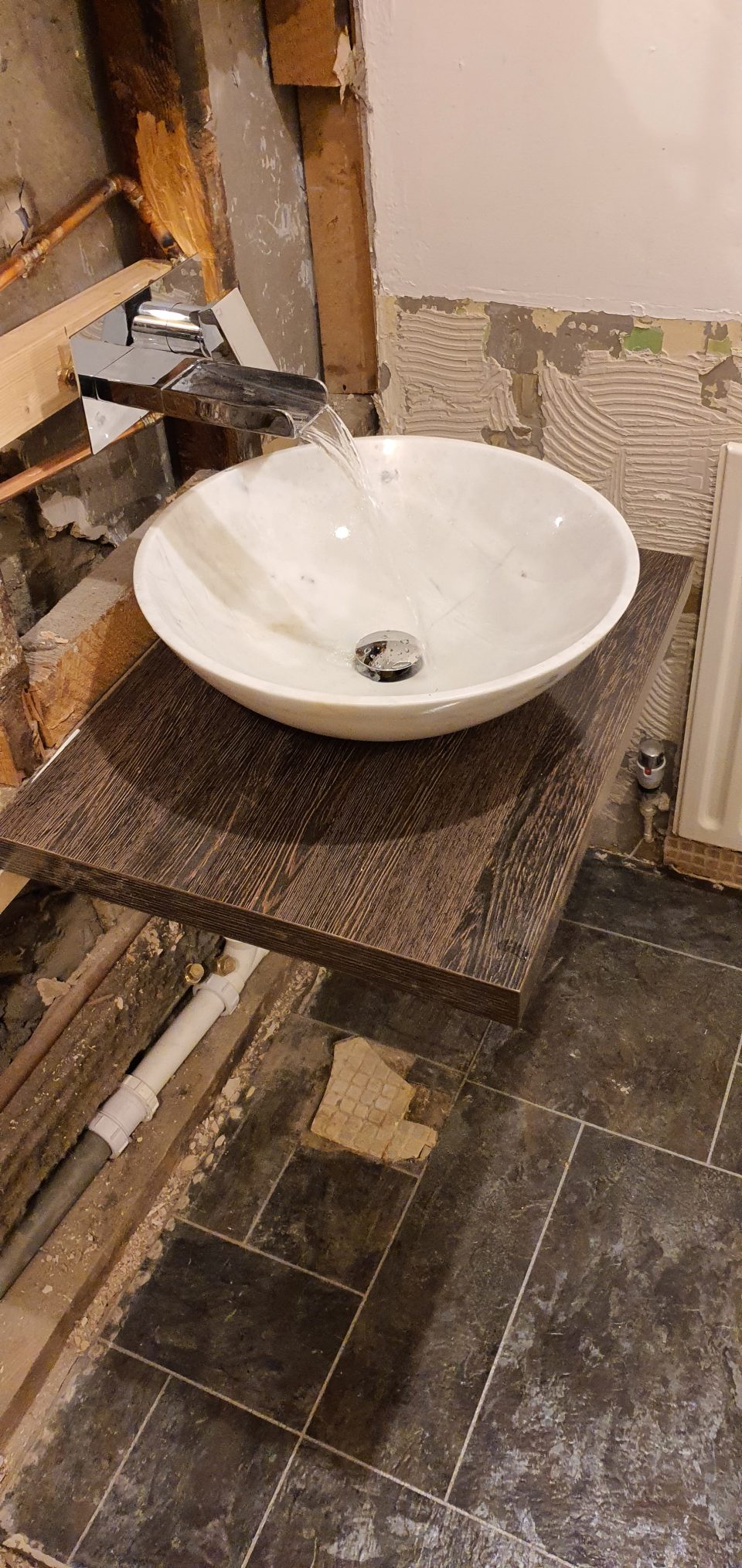 Fitting: the marble bowl basin and waterfall tap set on a floating shelf against the new grey tiling.
