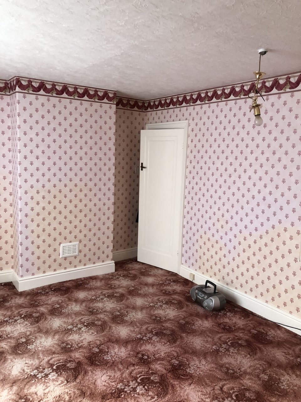 The bedroom before work — dated pink floral wallpaper, old carpet and a tired ceiling.