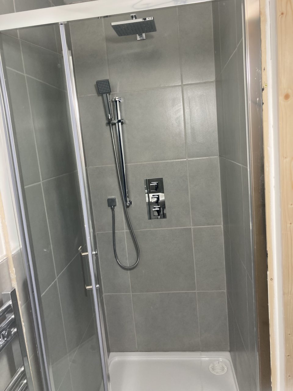 The finished en-suite — vanity basin and a heated towel rail, fully tiled in grey.