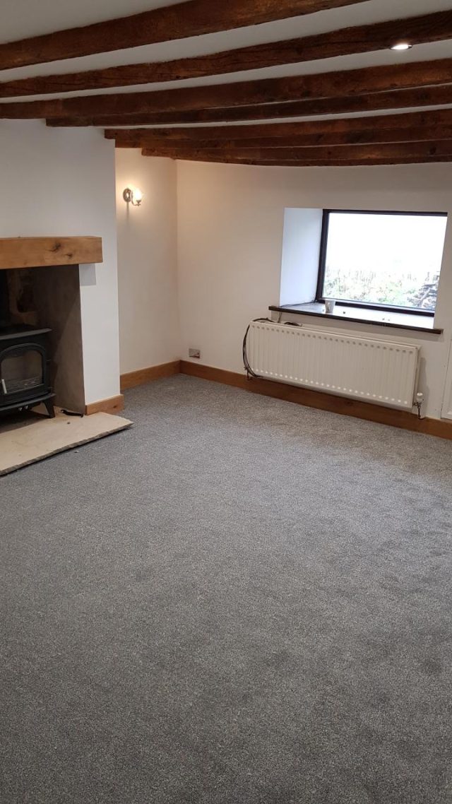 The finished living room with new grey carpet laid, oak skirting and the original beams overhead.