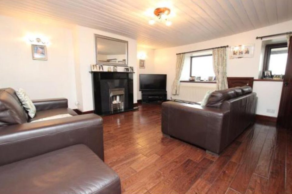 The cottage living room before work — white tongue-and-groove panelled ceiling, a blocked tiled fireplace and a dark mahogany floor.