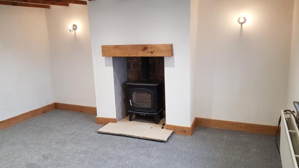 The finished fireplace — wood burner, exposed original stone and an oak mantel beam.