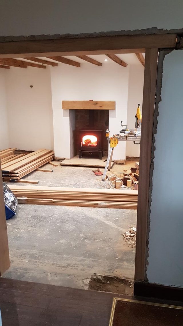 Mid-renovation: the lit wood burner with new oak skirting boards stacked ready to fit.