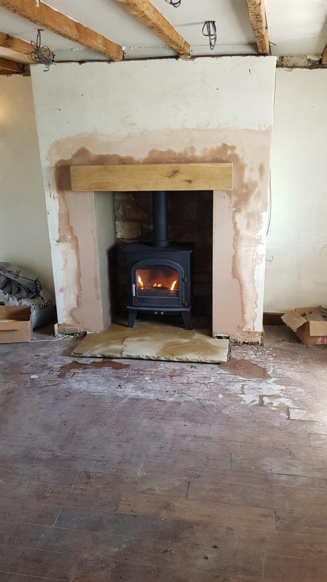 Fitting: the wood burner set on its stone hearth beneath a new oak beam mantel, walls freshly replastered.