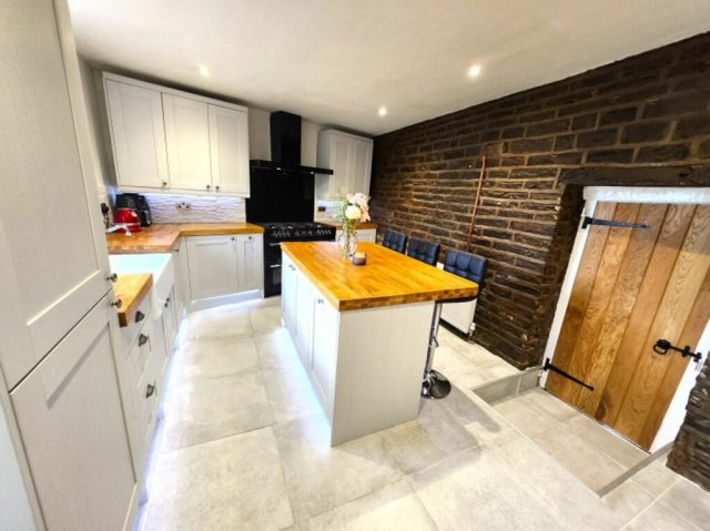 The finished kitchen from another angle — grey shaker units, oak worktops and the exposed brick wall.