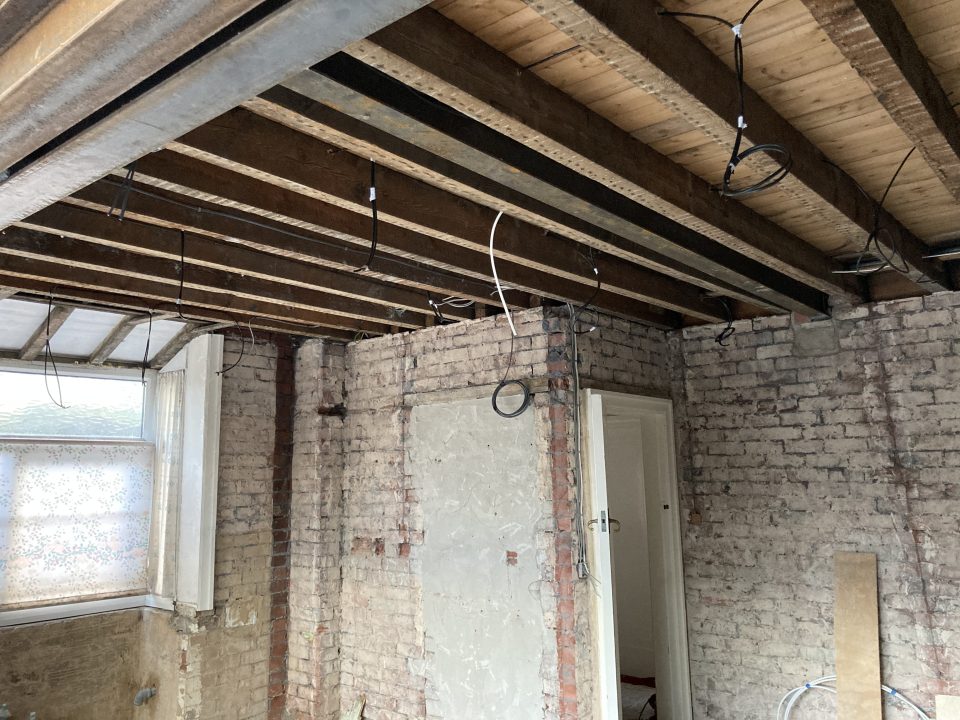 The extension as handed over by the structural contractor — a bare shell, back to brick and blockwork with the steels and joists exposed.