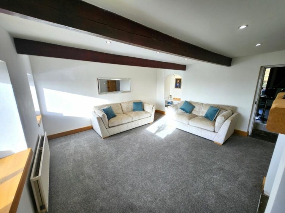 The finished living room — original ceiling beams kept, an oak mantel and brace-and-batten oak door, and a lighter grey carpet.
